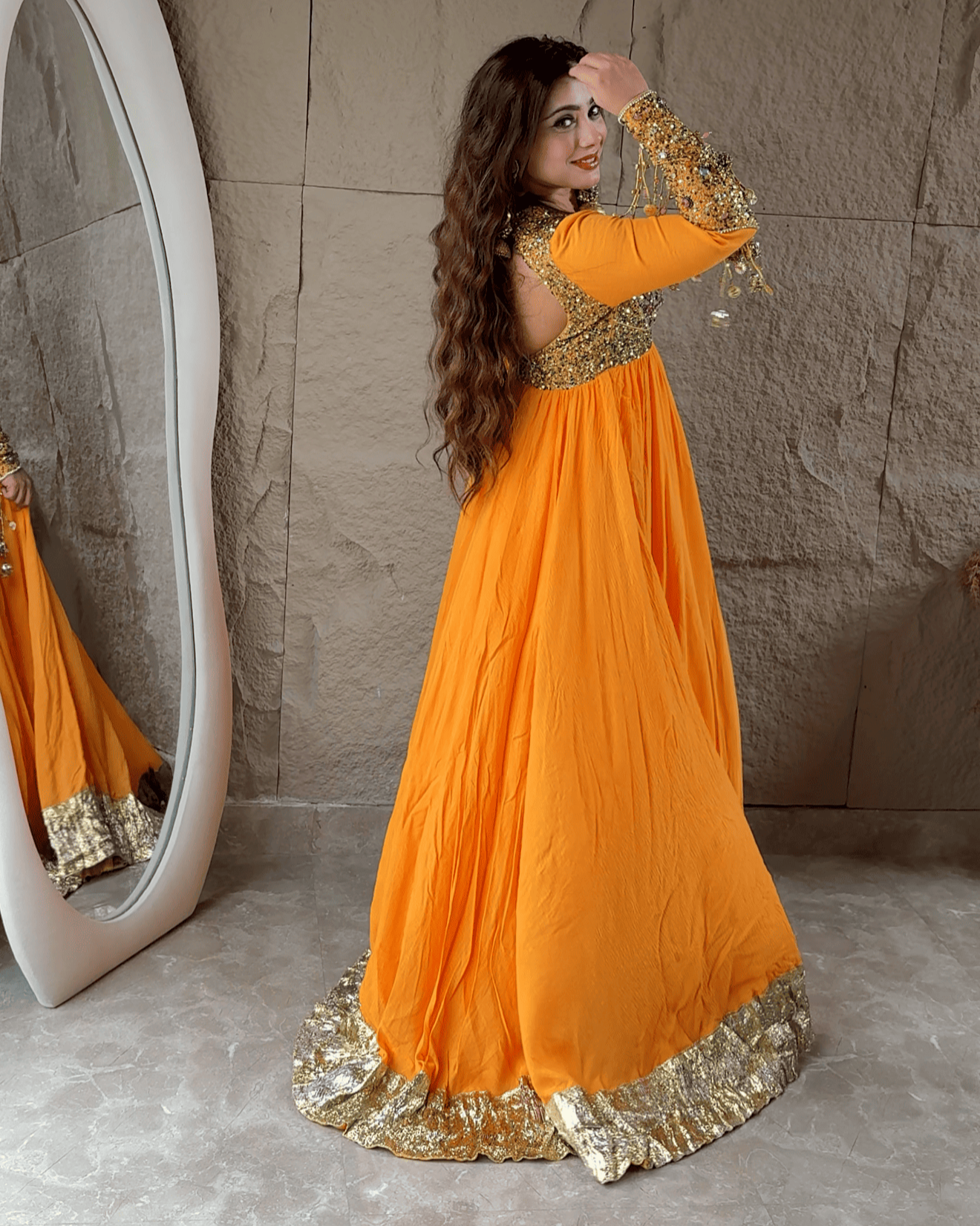 Woman in an orange and gold traditional outfit standing in front of a mirror.