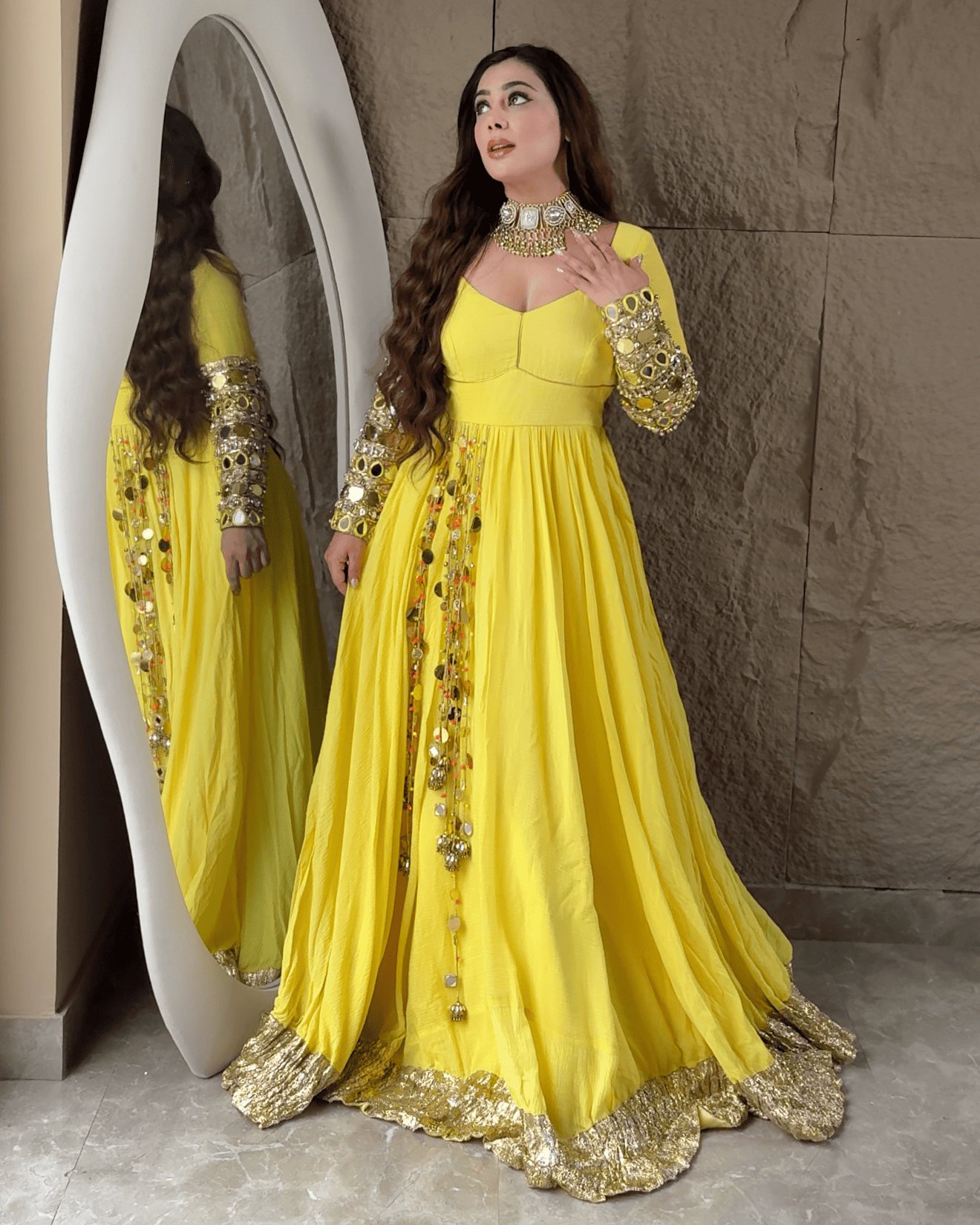 Woman in a yellow dress with gold embroidery standing in front of a mirror.