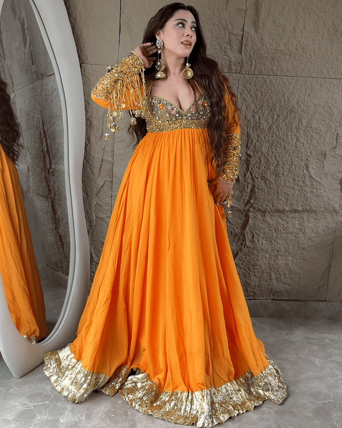 Woman in an orange and gold traditional outfit standing in front of a mirror.