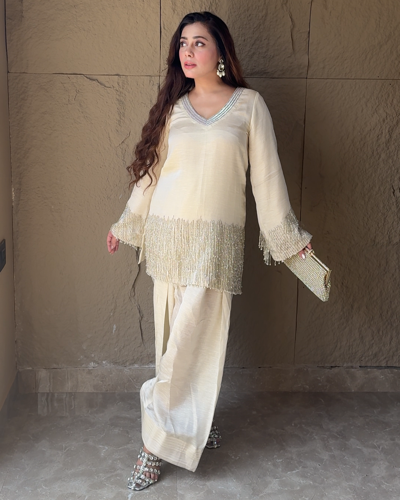 Woman in a cream-colored outfit standing against a textured wall.