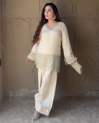 Woman in a cream-colored outfit standing against a textured wall.