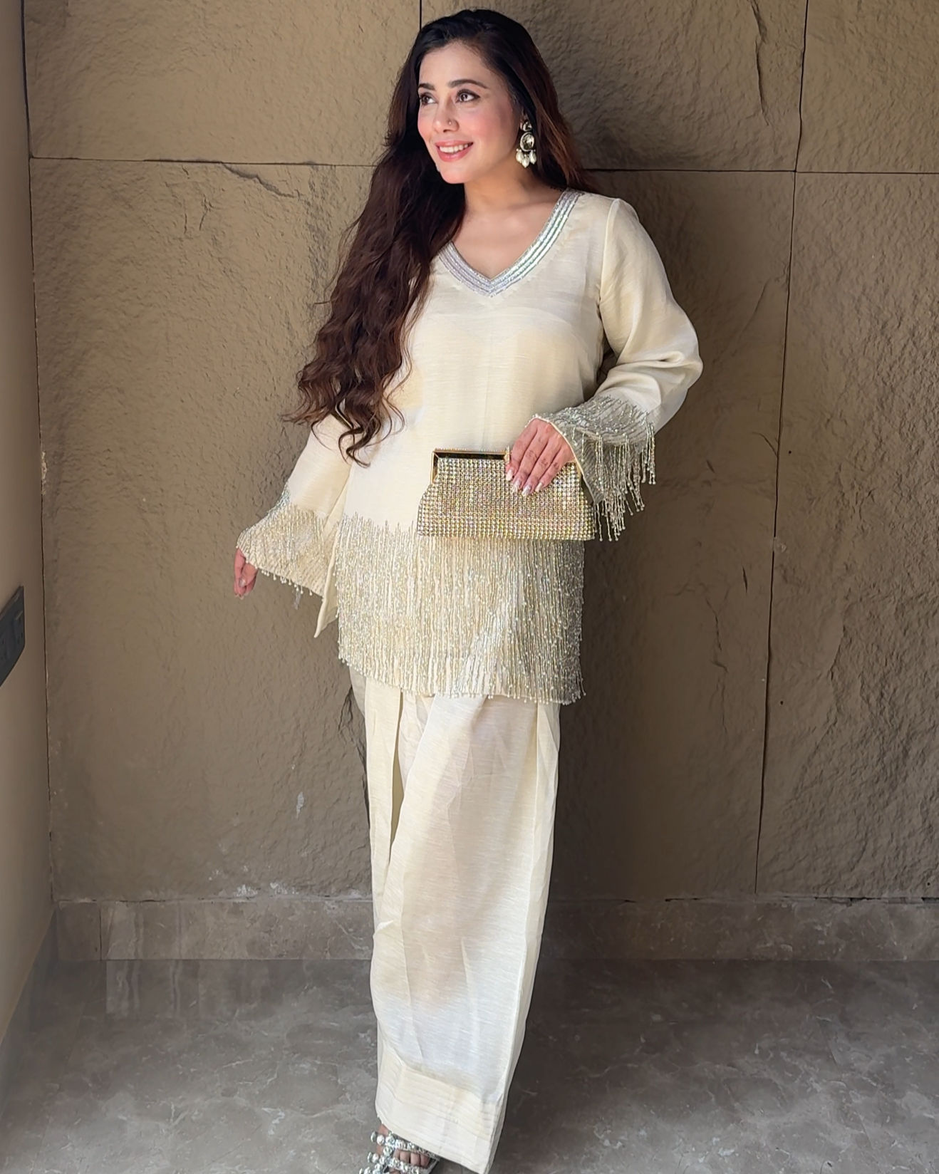 Woman in a cream-colored outfit with a matching handbag against a textured wall.