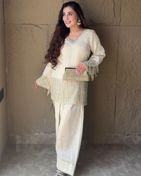 Woman in a cream-colored outfit with a matching handbag against a textured wall.
